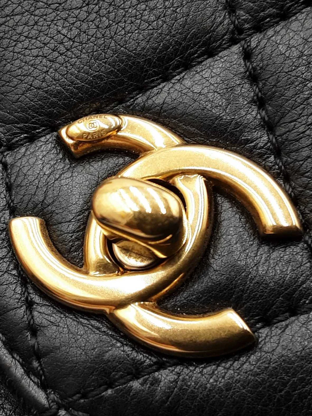 Close-up of authentic Chanel CC lock hardware on a black quilted leather Classic Flap bag.