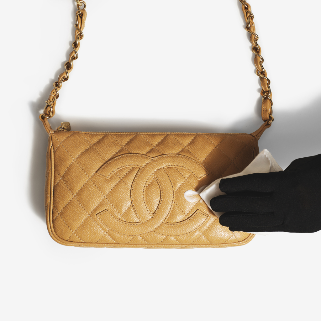 Expert cleaning a quilted leather designer bag with a microfiber cloth.